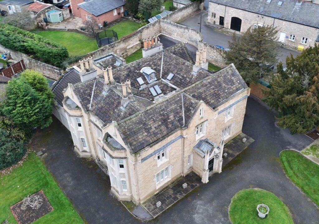 Aerial view of a historic stone building surrounded by green lawns