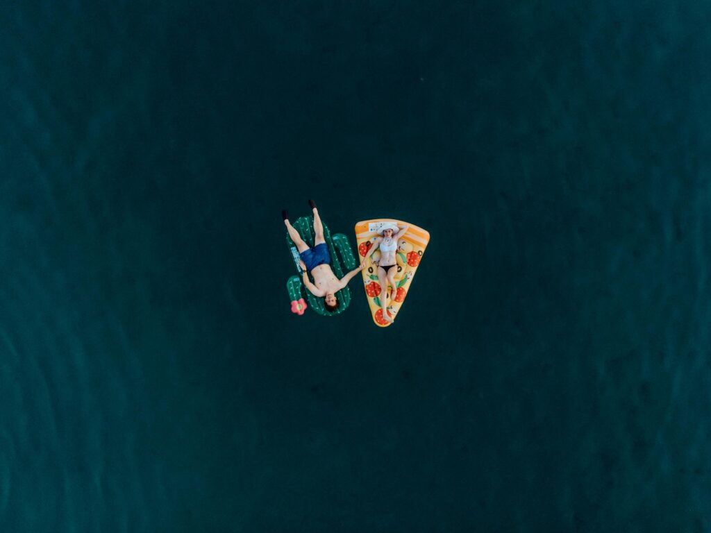 A lone paddleboarder on calm, deep blue water viewed from above